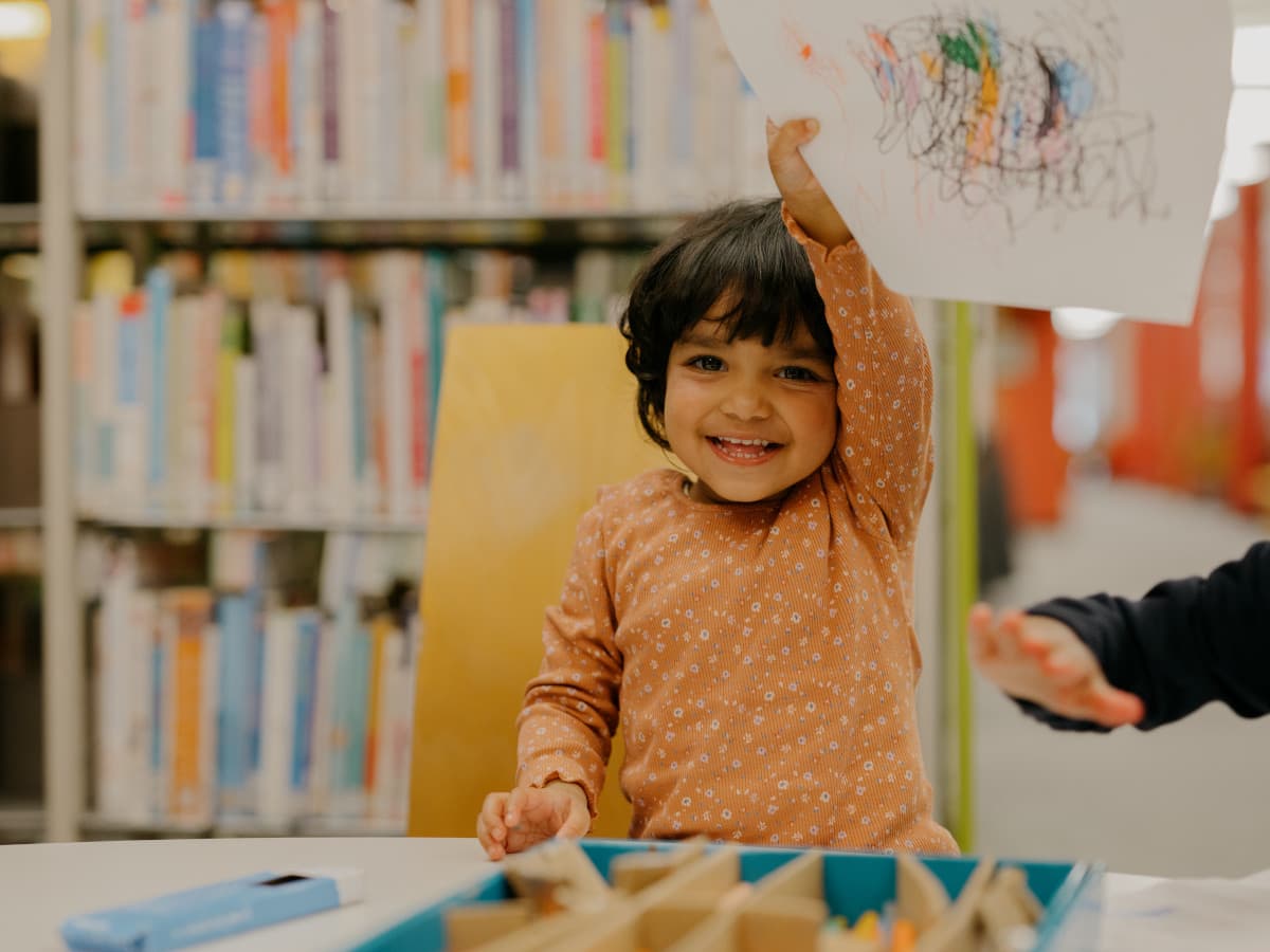 A little girl shows off her drawing at the library.