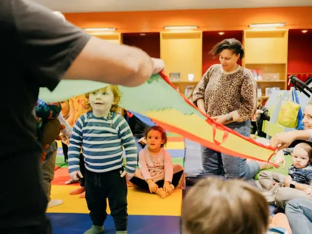 A little boy underneath a colourful canopy being held up by adults in the library.