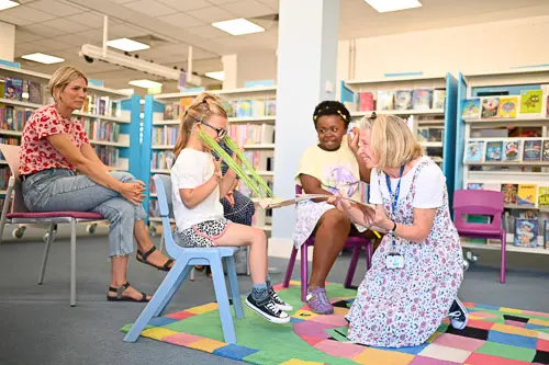 A member of library staff plays a game with children taking part in a multi-sensory storytime aimed at young people with additional needs. The librarian is using props and the children are smiling.