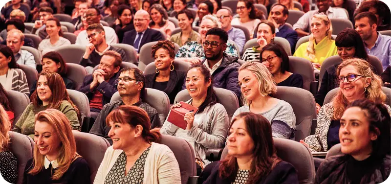 An audience sitting at a conference. The people are smiling and laughing.