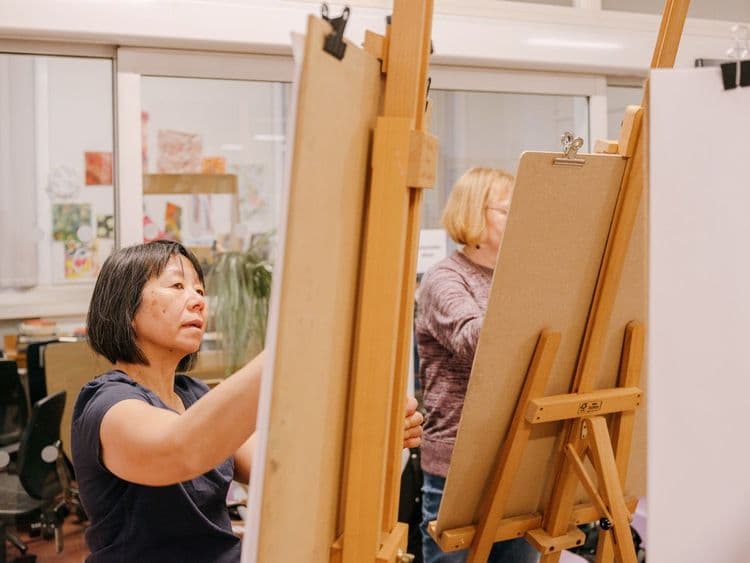 A lady painting on a canvas at a library art group. The canvas is on an easel.